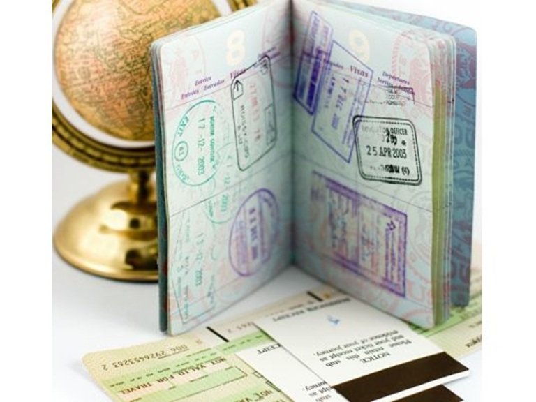 An open passport with multiple entry and exit stamps next to a small globe and travel documents